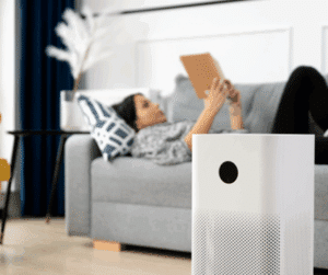 A woman lying on a couch reading a book with an air scrubber in the forefront