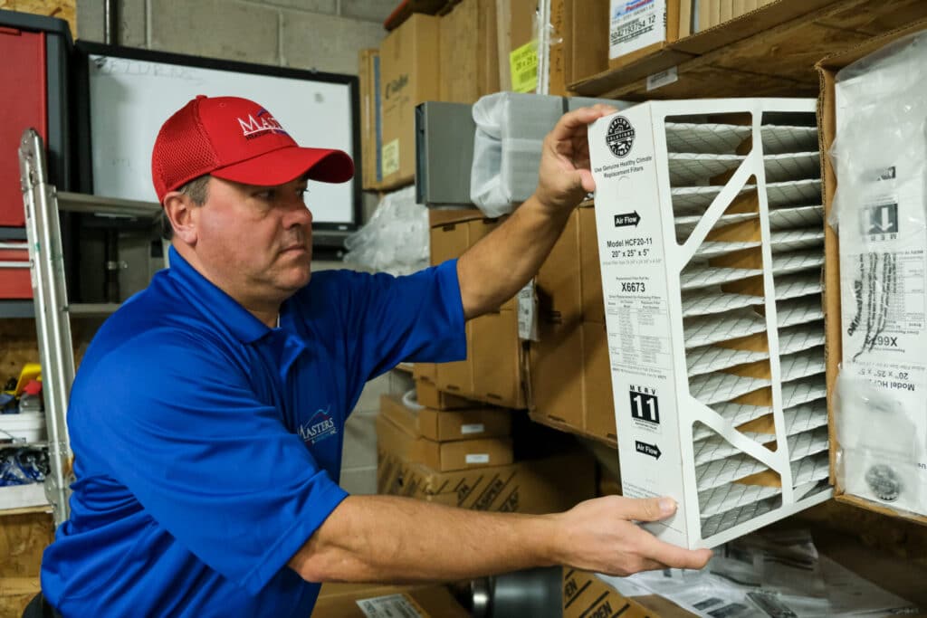 Masters Heating, Cooling, Plumbing & Electrical technician preparing for an AC repair service appointment by getting a new air filter off the shelf