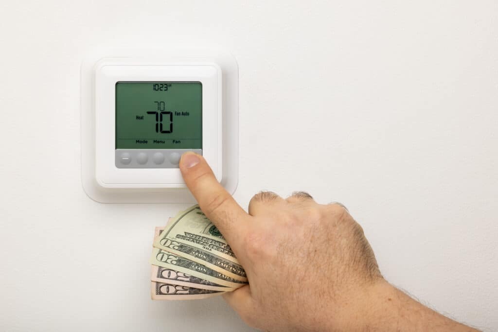 Hand holding cash while adjusting thermostat