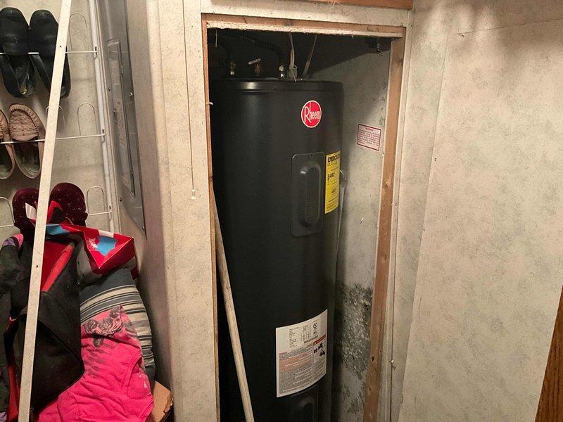 Responded to service call for leaking electric tanked water heater located in basement utility area. Upon arrival, assessed the unit installed in framed opening adjacent to storage space. Took measurements of clearance space and documented existing water heater configuration, including manufacturer specifications and energy guide labels. Photographed unit condition and surrounding installation area to document leak source and determine replacement requirements.