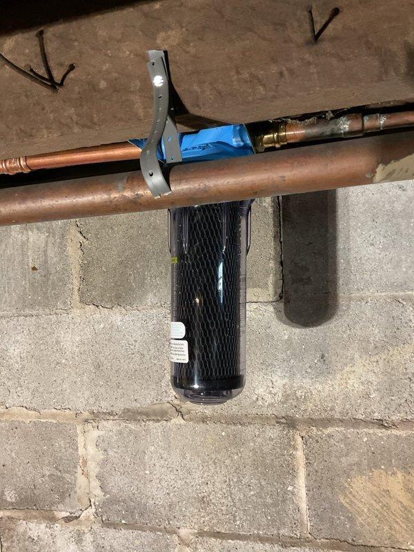 Completed replacement of two water filtration cartridges on existing whole-house water treatment system installed in basement utility area. Removed old filter elements from clear housings mounted on copper supply lines beneath floor joists. Installed new carbon block filter cartridges, ensuring proper seating and O-ring placement. Verified all brass fittings and connections were secure at filter head assemblies with blue caps. Pressurized system and checked for leaks at housing seals and pipe connections. Confirmed proper water flow through filters and verified system operation with no signs of bypass or leakage.