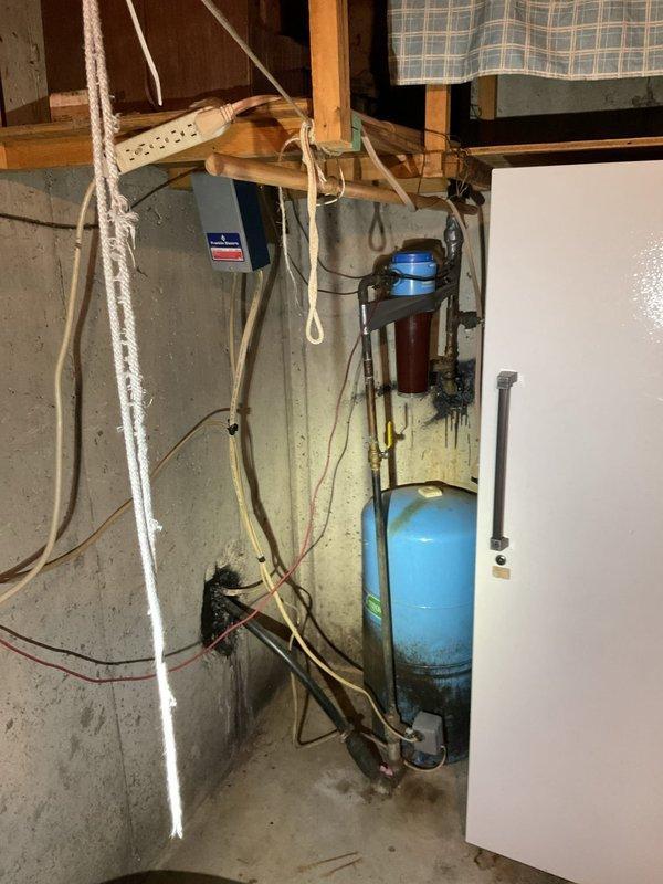 Responded to customer complaint of fluctuating water pressure and unusual noises coming from well pressure tank in basement. Upon inspection, confirmed presence of 40+ year old blue pressure tank showing significant age-related wear and surface deterioration. Diagnosed failed bladder in pressure tank based on observed symptoms including pressure fluctuations and audible noise during system operation. Documented existing well system configuration including pressure tank, water treatment components, copper and PVC piping, filter housing, and associated valves and fittings mounted on concrete basement wall. Photographed complete installation for customer records showing tank condition, plumbing connections, and overall system layout. Provided assessment of tank failure and recommended replacement of aging pressure tank to restore proper system function and maintain consistent water pressure throughout residence.