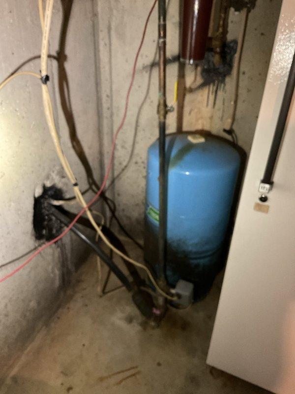 Responded to customer complaint of fluctuating water pressure and unusual noises coming from well pressure tank in basement. Upon inspection, confirmed presence of 40+ year old blue pressure tank showing significant age-related wear and surface deterioration. Diagnosed failed bladder in pressure tank based on observed symptoms including pressure fluctuations and audible noise during system operation. Documented existing well system configuration including pressure tank, water treatment components, copper and PVC piping, filter housing, and associated valves and fittings mounted on concrete basement wall. Photographed complete installation for customer records showing tank condition, plumbing connections, and overall system layout. Provided assessment of tank failure and recommended replacement of aging pressure tank to restore proper system function and maintain consistent water pressure throughout residence.