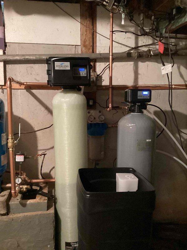 Completed full-day installation of comprehensive water treatment system including water softener, filtration unit, and 20-gallon ProFlo PFX20S well pressure tank. All components were professionally mounted to basement wall with proper copper piping connections, brass valve assemblies, and blue filter housing, with black containment drip pan installed at base to protect against potential leaks.