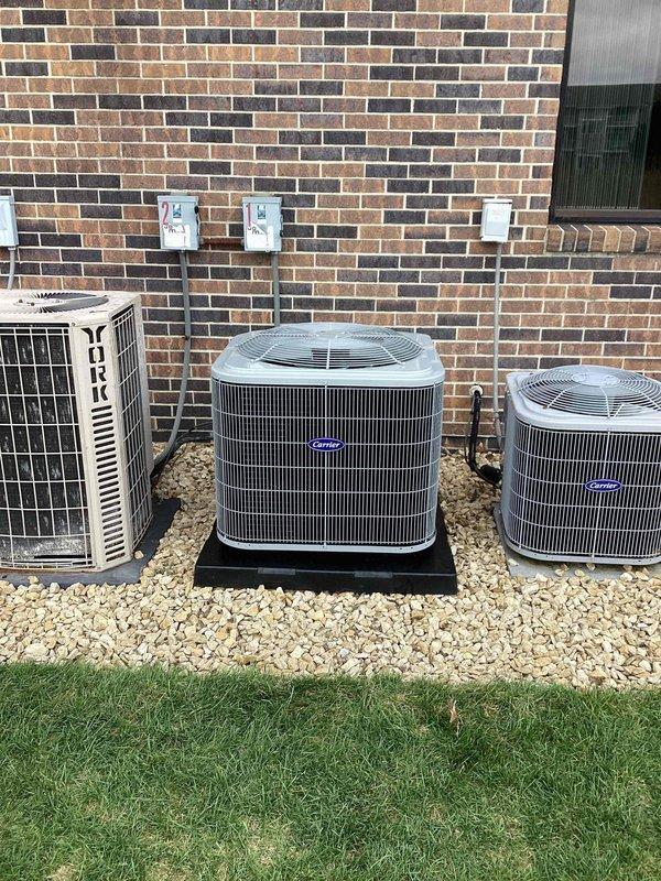 # HVAC Install - Complete System - Commercial

Completed full commercial HVAC system installation including multiple outdoor condensing units and associated indoor mechanical components. Installed three exterior condenser units against building perimeter, consisting of one York unit with protective cage enclosure and two additional condensing units mounted on equipment pads with proper gravel base for drainage and stability. All exterior units positioned to ensure adequate airflow clearance and service access.

Interior installation included complete mechanical room setup with new water heater tank, copper and PVC supply lines, gas piping distribution system with shut-off valves, and pressure relief components. Installed furnace unit with proper venting and integrated all plumbing connections including hot and cold water distribution manifolds. All piping secured with appropriate hangers and supports per code requirements. System includes multiple zone control valves and isolation poin