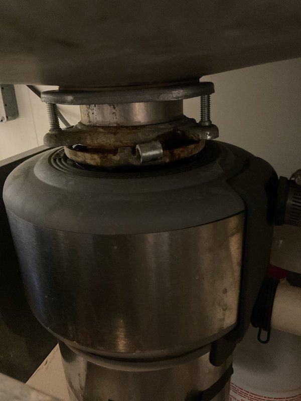 Angola, IN - Responded to commercial bathroom water leak at fitting underneath sink. Upon inspection, identified leak source at garbage disposal mounting assembly connection point. Tightened mounting hardware and inspected disposal unit for additional issues, noting corrosion and age-related wear on metal components and mounting ring assembly.