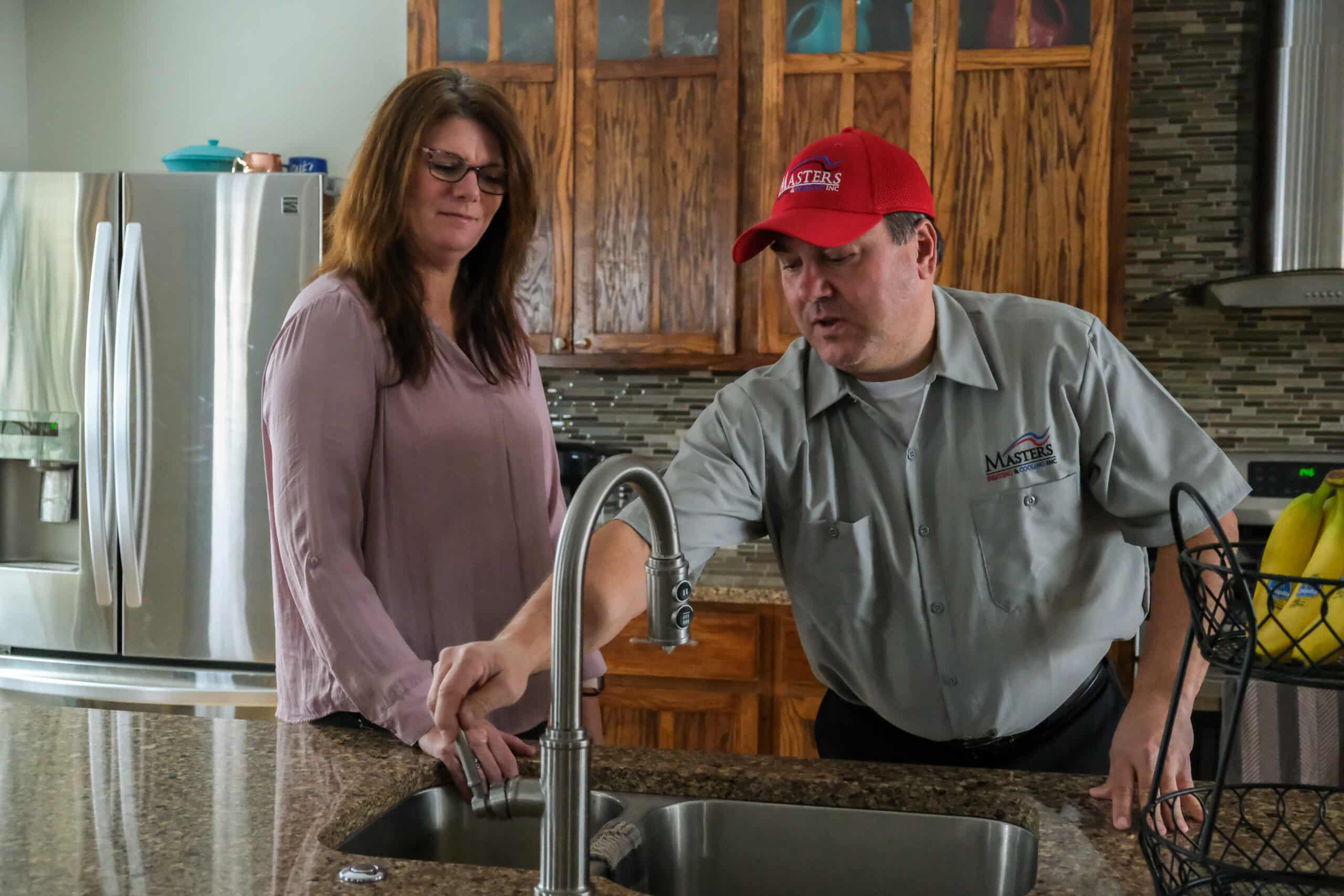 Masters Heating & Cooling team member showing homeowner kitchen sink after install